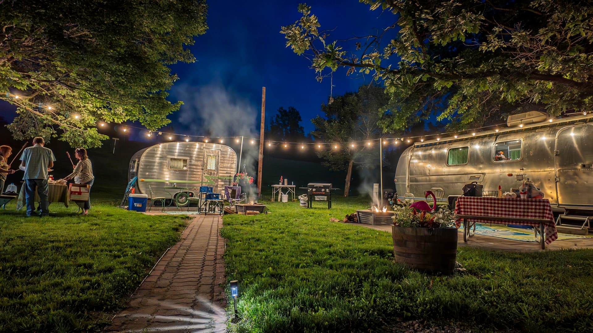 Vintage glamping campers lit up at night with string lights and fire pits