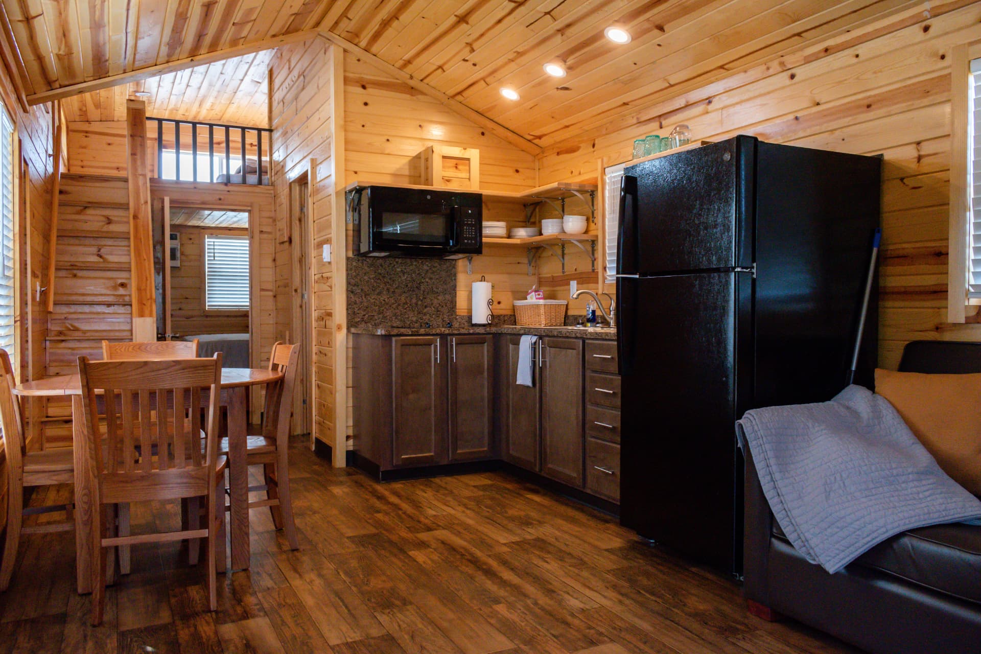 Knotty pine cabin interior with kitchenette, dining area, and loft sleeping area at Alta Campground