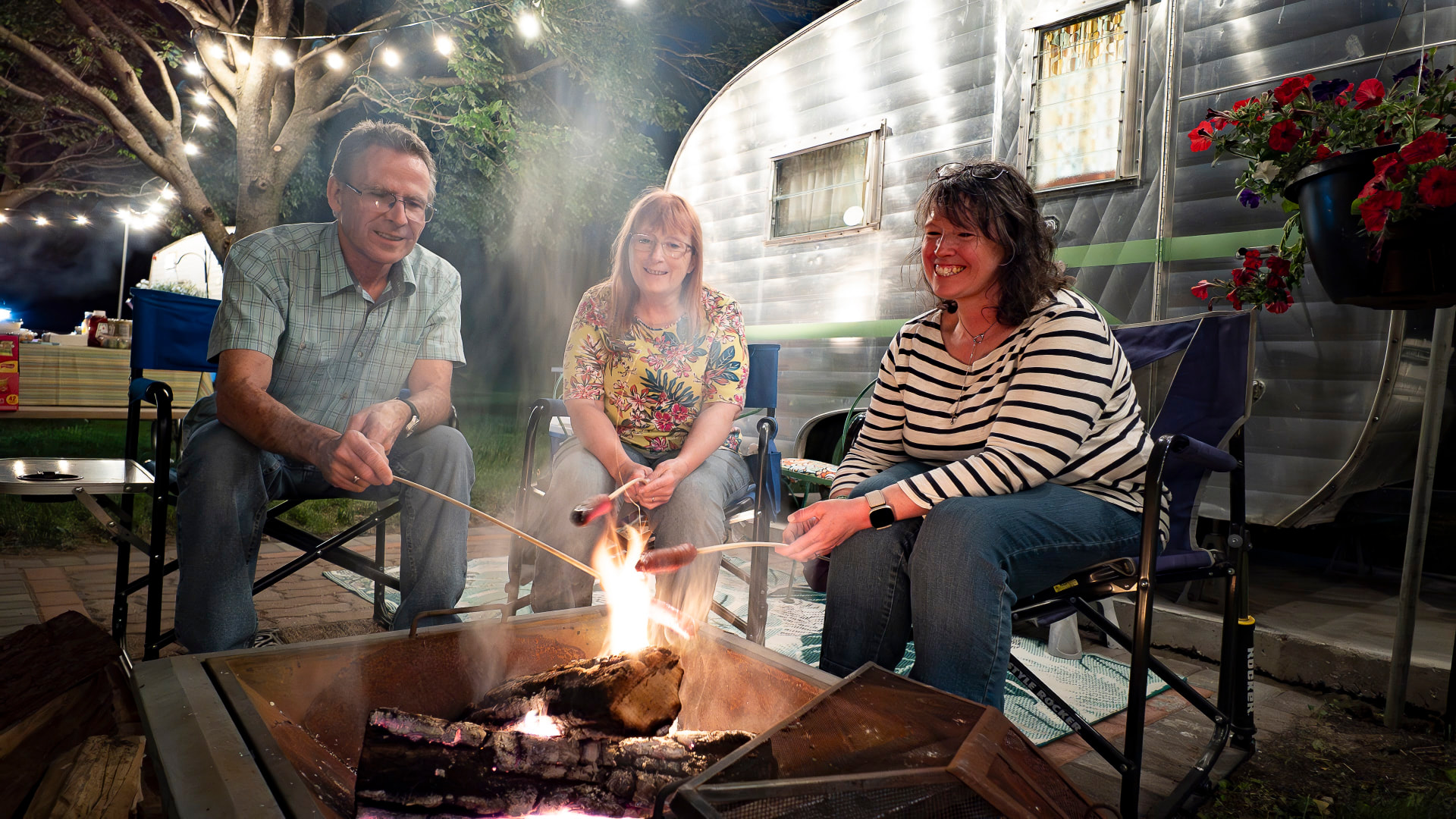 Friends gathered around a fire pit by a vintage camper at night